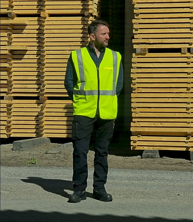 Filip Ridefors i varselväst framför staplat virke på en arbetsplats